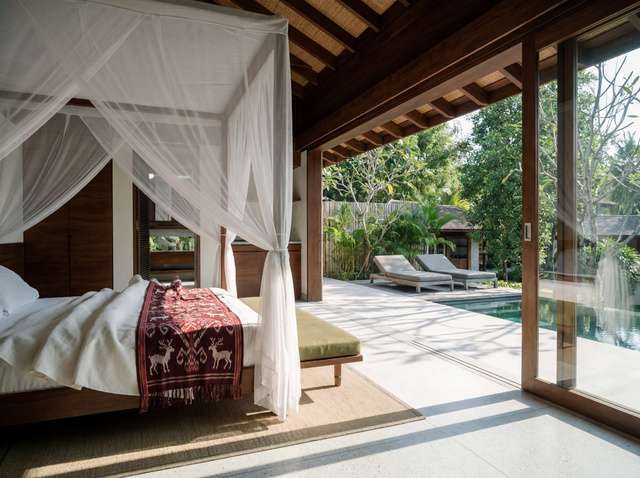 Sunlit four-poster canopy bedroom opening onto private pool terrace with authentic Sumba Ikat textiles